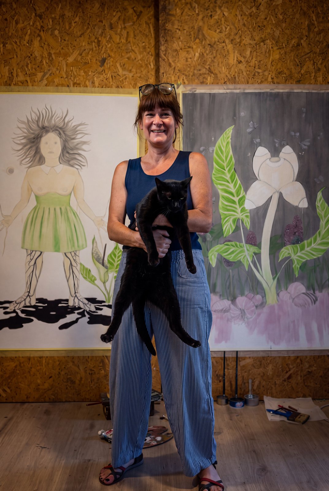 Banu Birecikligil mit ihrer schwarzen Katze im Atelier, im Hintergrund zwei großformatige Arbeiten